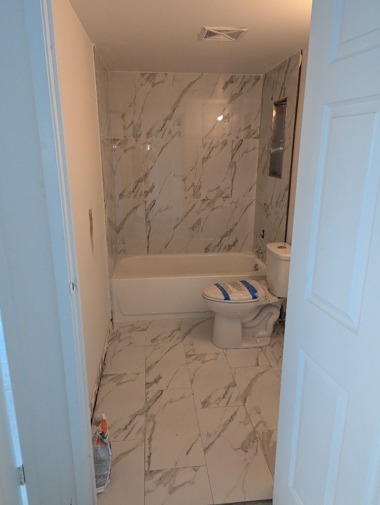 Bathroom under construction with marble-look tile. White tub, toilet, and walls. Doorway on the right.
