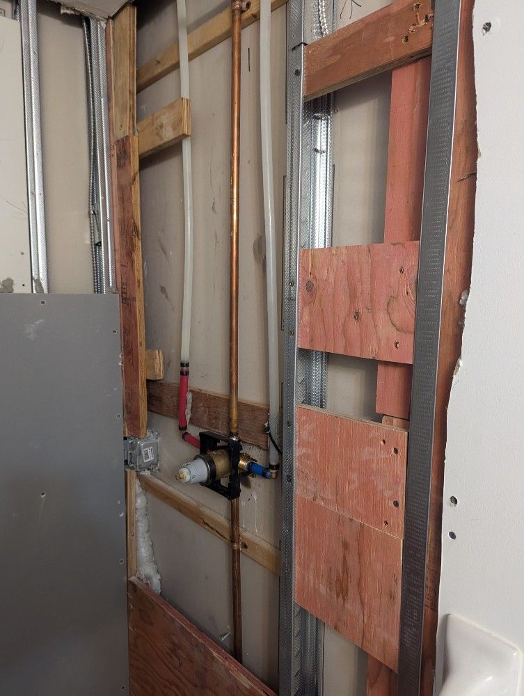 Bathroom wall under construction showing plumbing pipes and wooden framing.