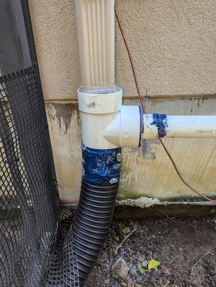 Downspout connected to a corrugated drain pipe, wrapped in blue tape, next to a building.