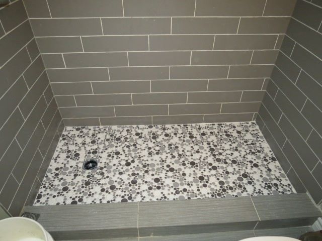 Gray tiled shower with patterned floor, low curb, and dark drain.