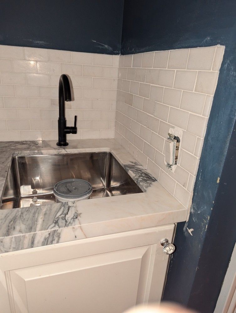 Kitchen sink with subway tile backsplash and dark faucet against a blue wall.