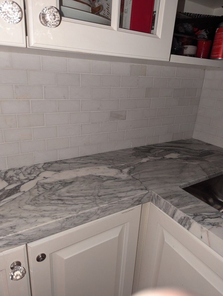 White kitchen with marble countertops, subway tile backsplash, and white cabinets.