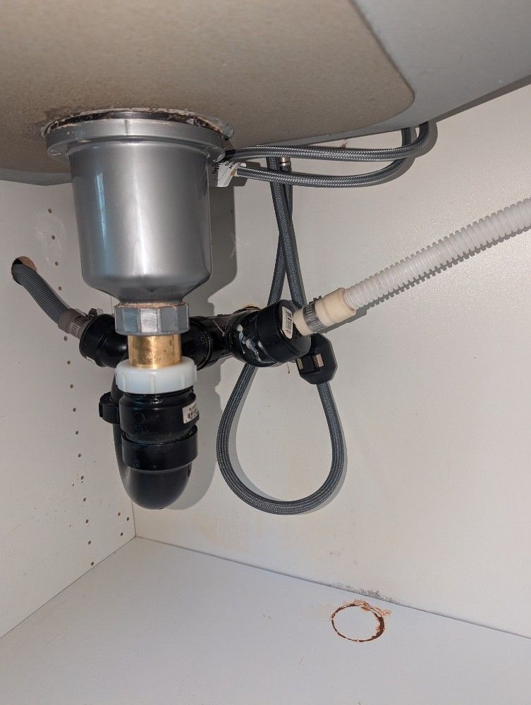 Underside of a kitchen sink with plumbing: garbage disposal, drain pipes, and a black P-trap.