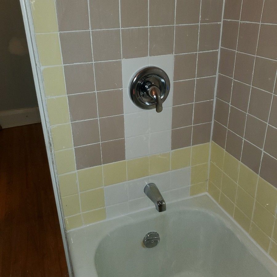Bathtub with tan, white, and yellow tiled walls, chrome fixtures.