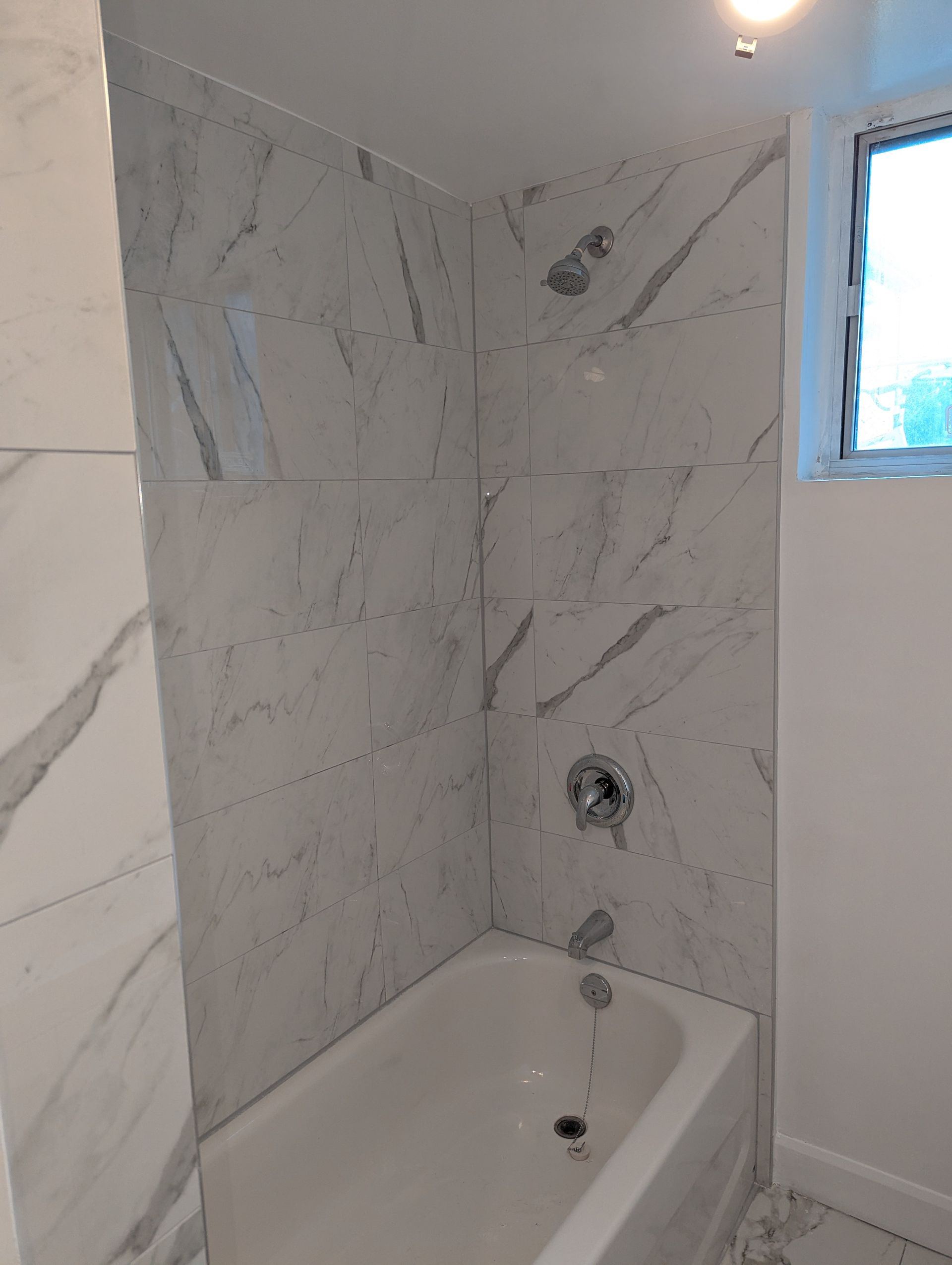 White marble tiled shower enclosure with a bathtub and chrome fixtures.