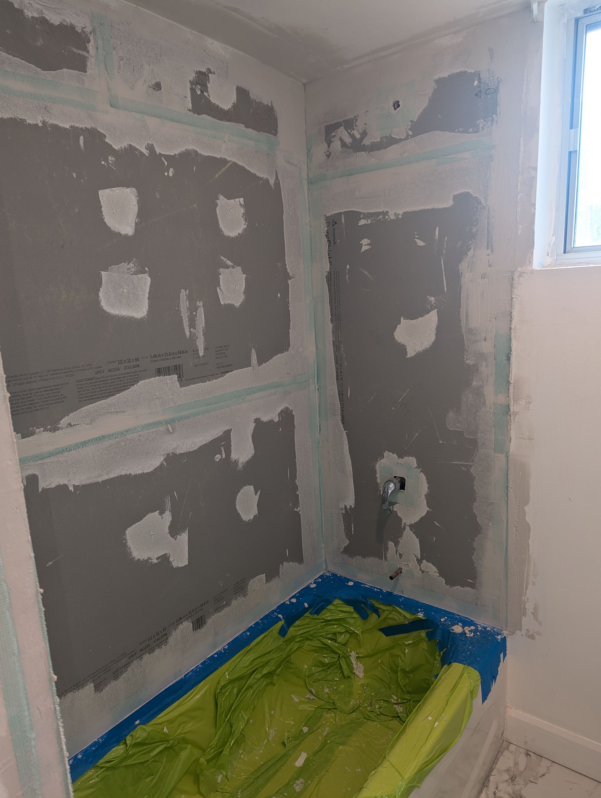 Bathroom wall with gray waterproofing, showing shower construction. A green cover protects the tub.