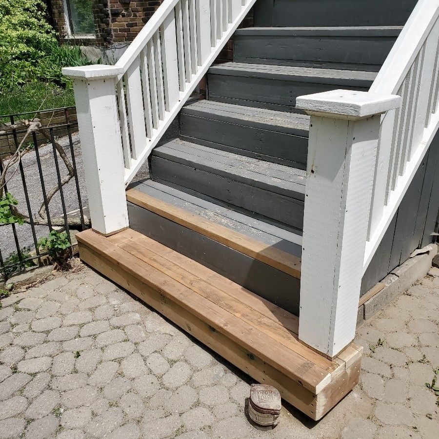 Outdoor stairway with gray steps and white railing. A wooden platform is at the base.