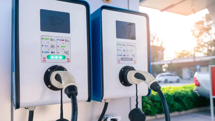 Electric vehicle charging stations with cords plugged in, outdoors.