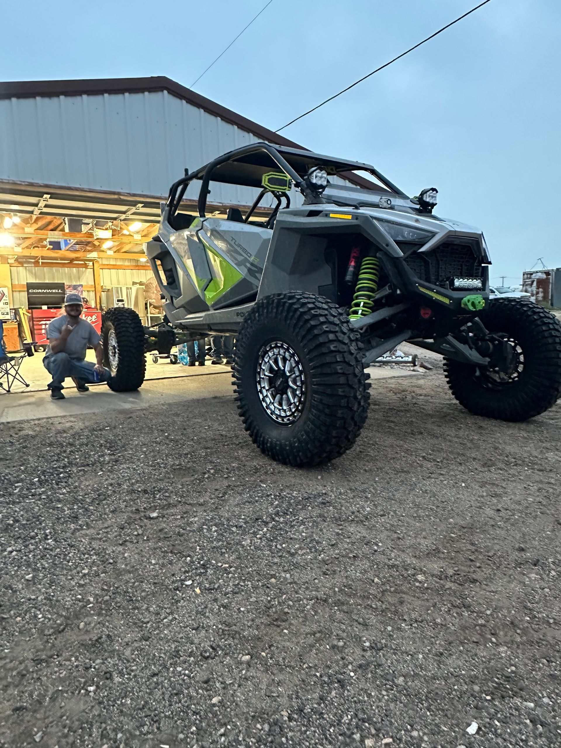 Off-road side-by-side buggy with large tires parked outside a garage at dusk