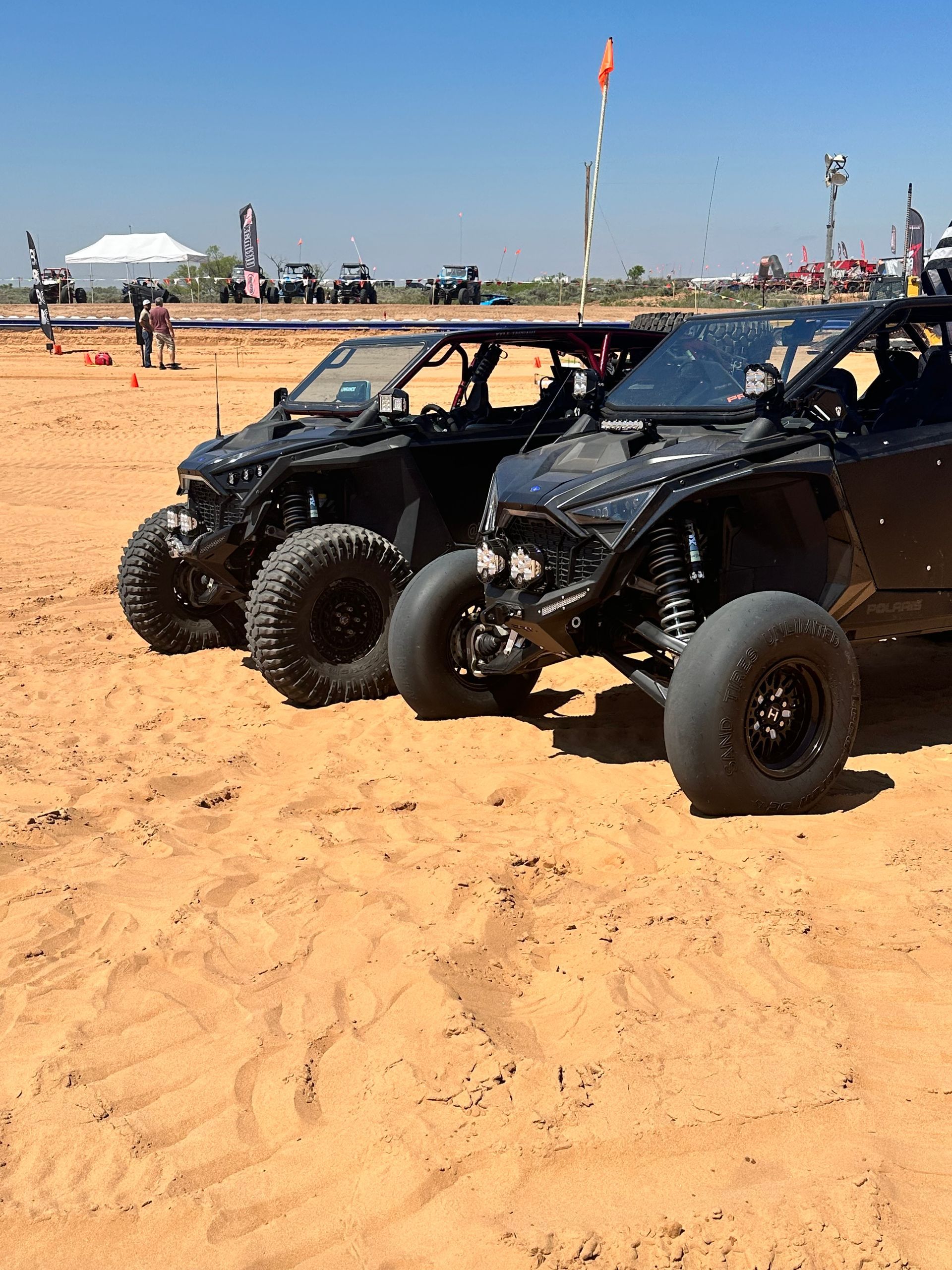 Two black off-road dune buggies parked on sandy terrain at an outdoor event