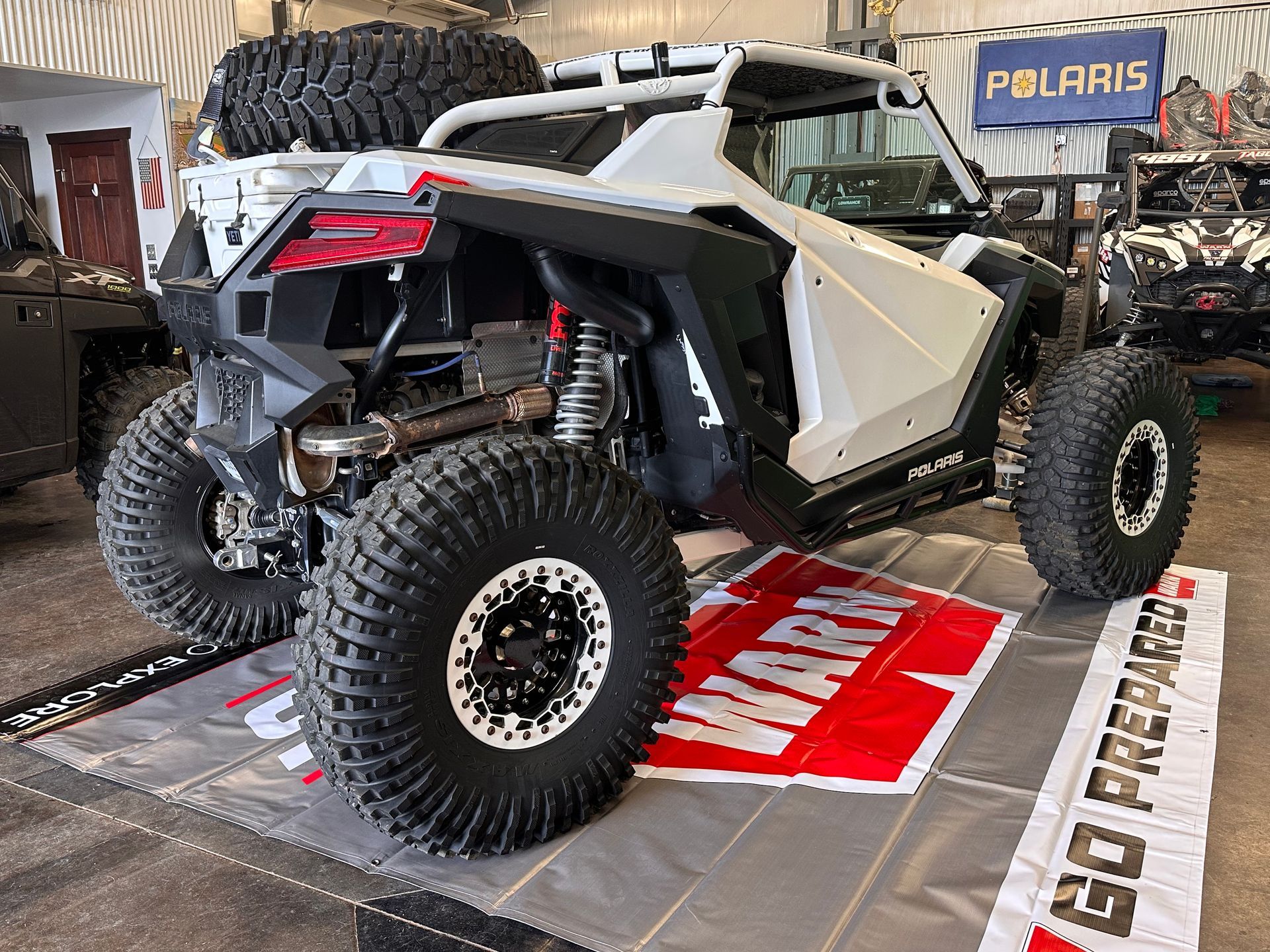 White Polaris off-road side-by-side parked in a garage showroom with large tires and roll cage