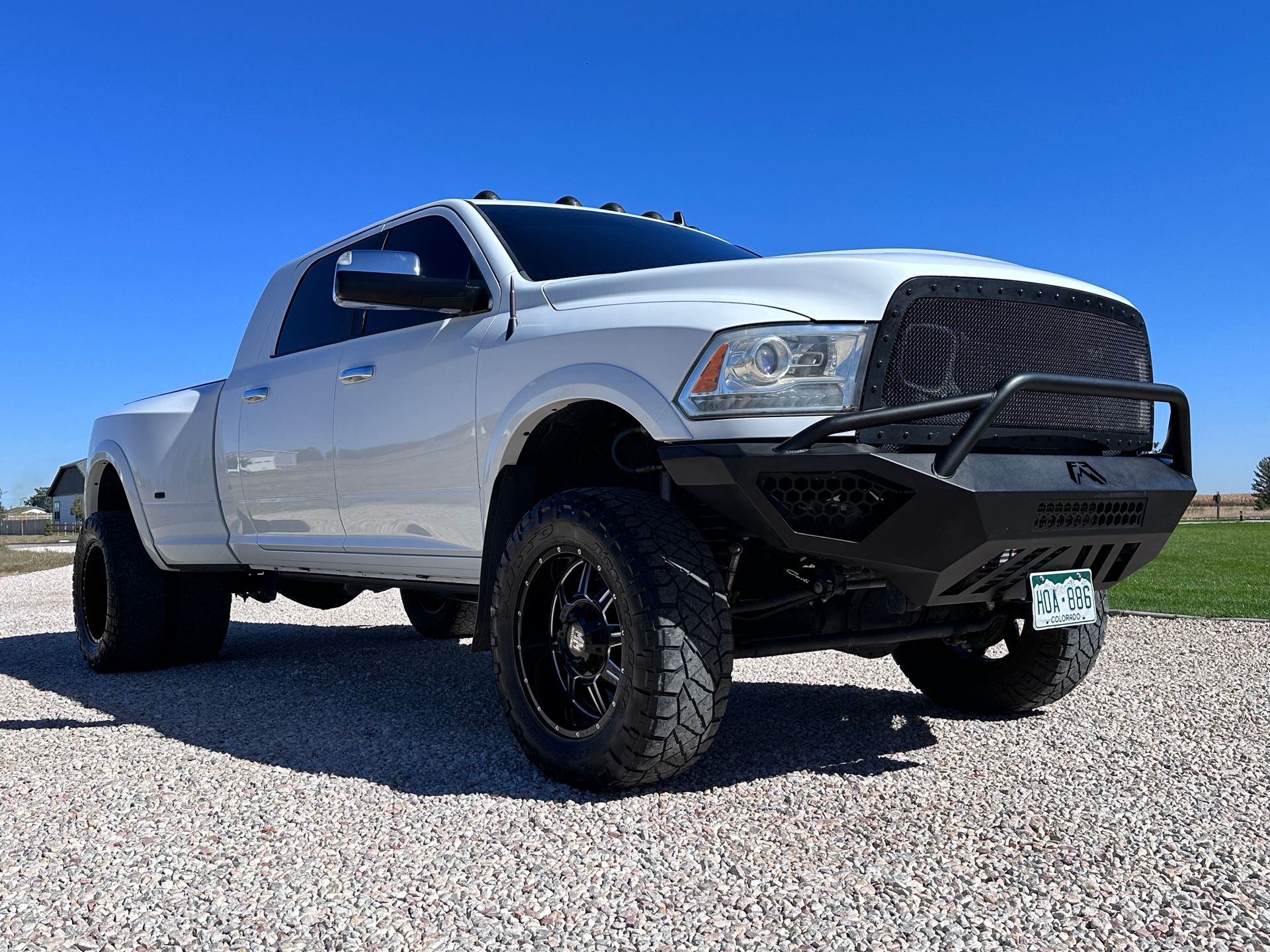 White lifted pickup truck with black rims parked on gravel under a clear blue sky