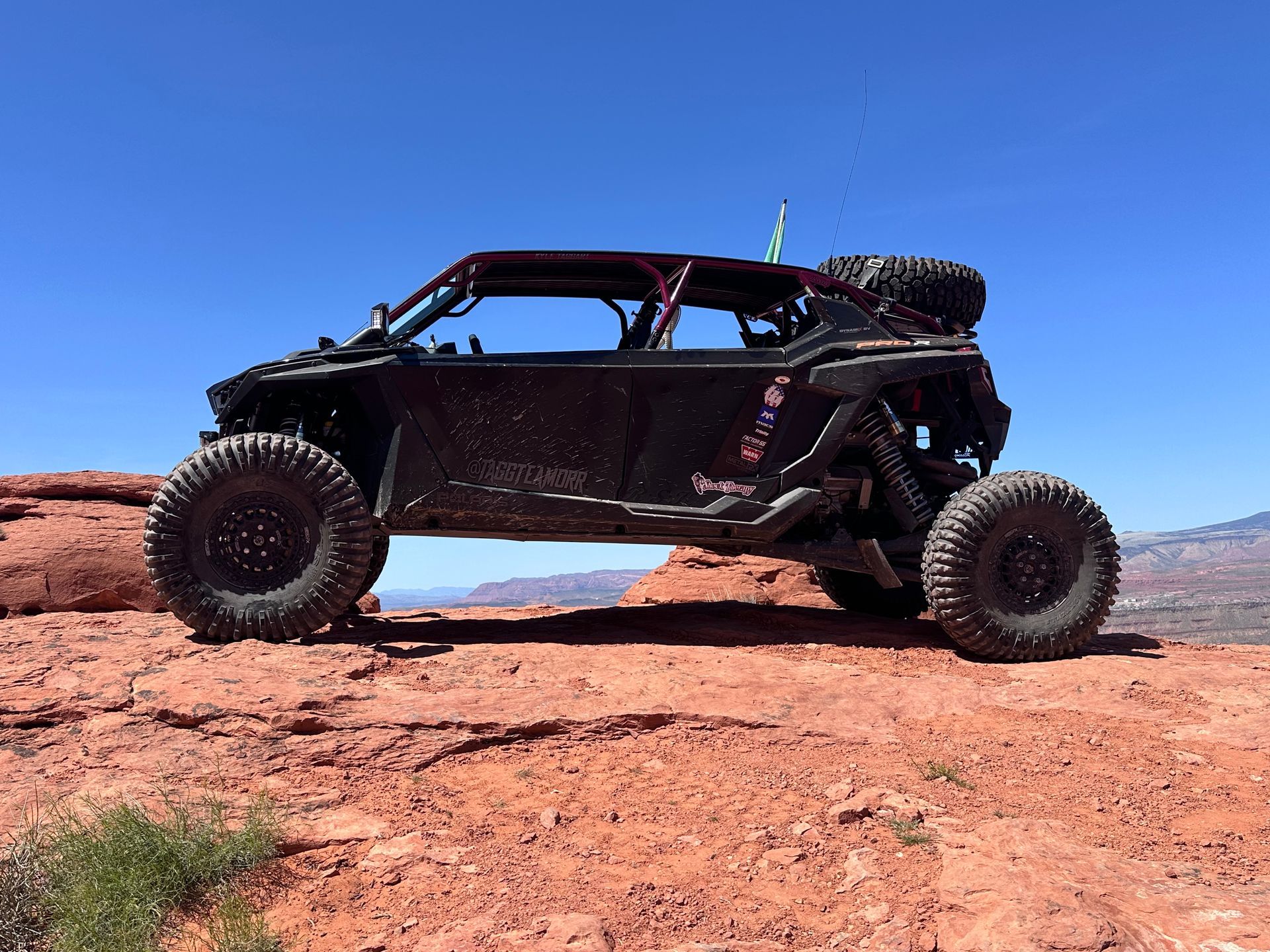 Black off-road rock crawler on red desert rocks under a clear blue sky.