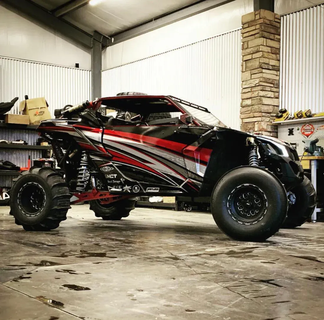 Black-and-red off-road buggy in a garage, viewed from the side on large tires.