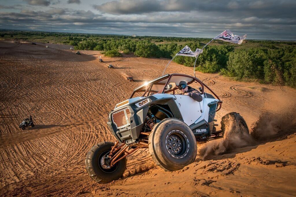 Off-road dune buggy racing across a sandy desert, kicking up dust under a cloudy sky