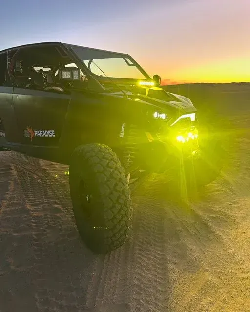 Off-road side-by-side at sunset with bright yellow headlights on a sandy trail