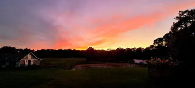 Sunset over a field and small building, with vibrant orange and purple colors in the sky.