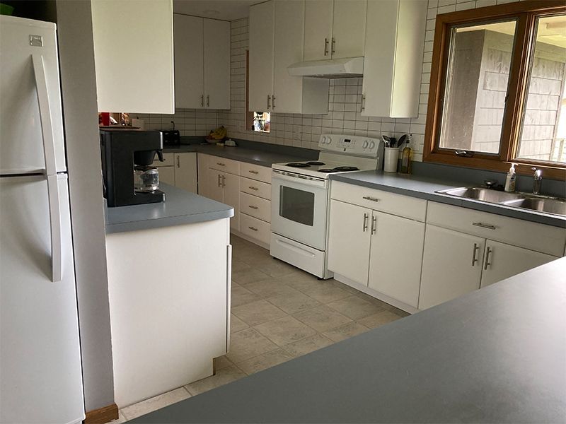 White kitchen with gray countertops, white appliances, and a window.