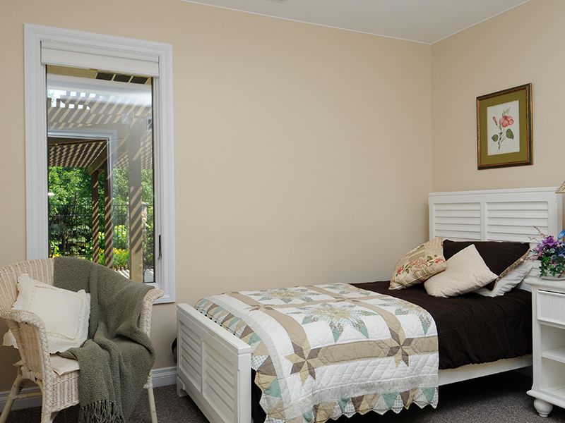 Bedroom with a bed, chair, and a window. Tan walls, white bedframe, and a quilt.