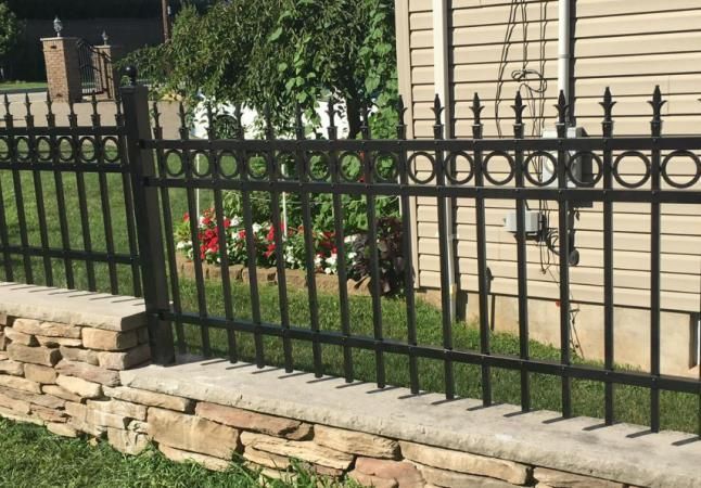 A black metal fence surrounds a stone wall in front of a house.