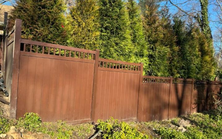 A wooden fence is surrounded by trees in a yard.