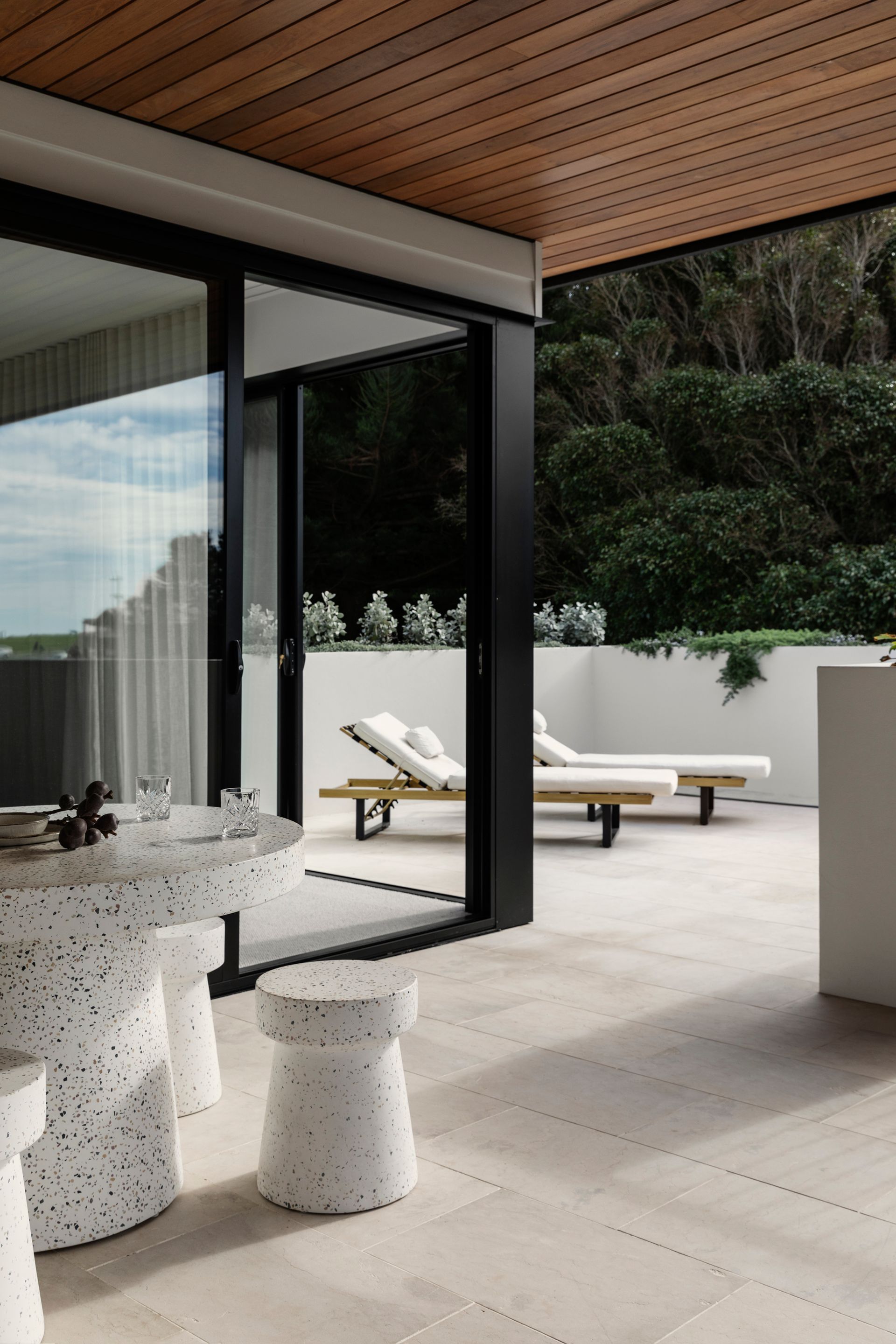 Patio with modern furniture, sliding glass doors, and a forest backdrop — Escarpment Building in Austinmer, NSW