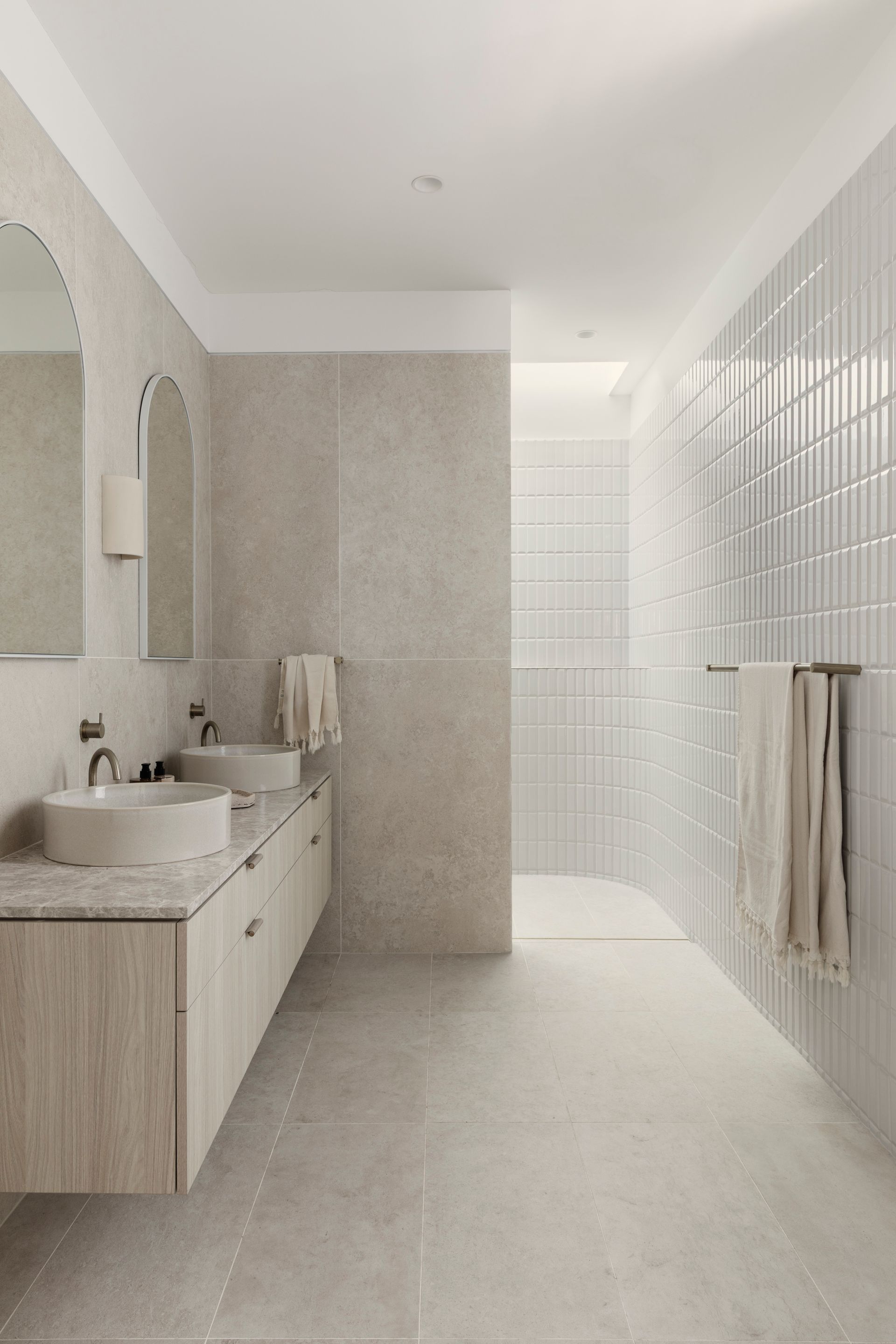 Modern bathroom with light wood vanity, two sinks, arched mirrors, and tiled shower — Escarpment Building in Austinmer, NSW