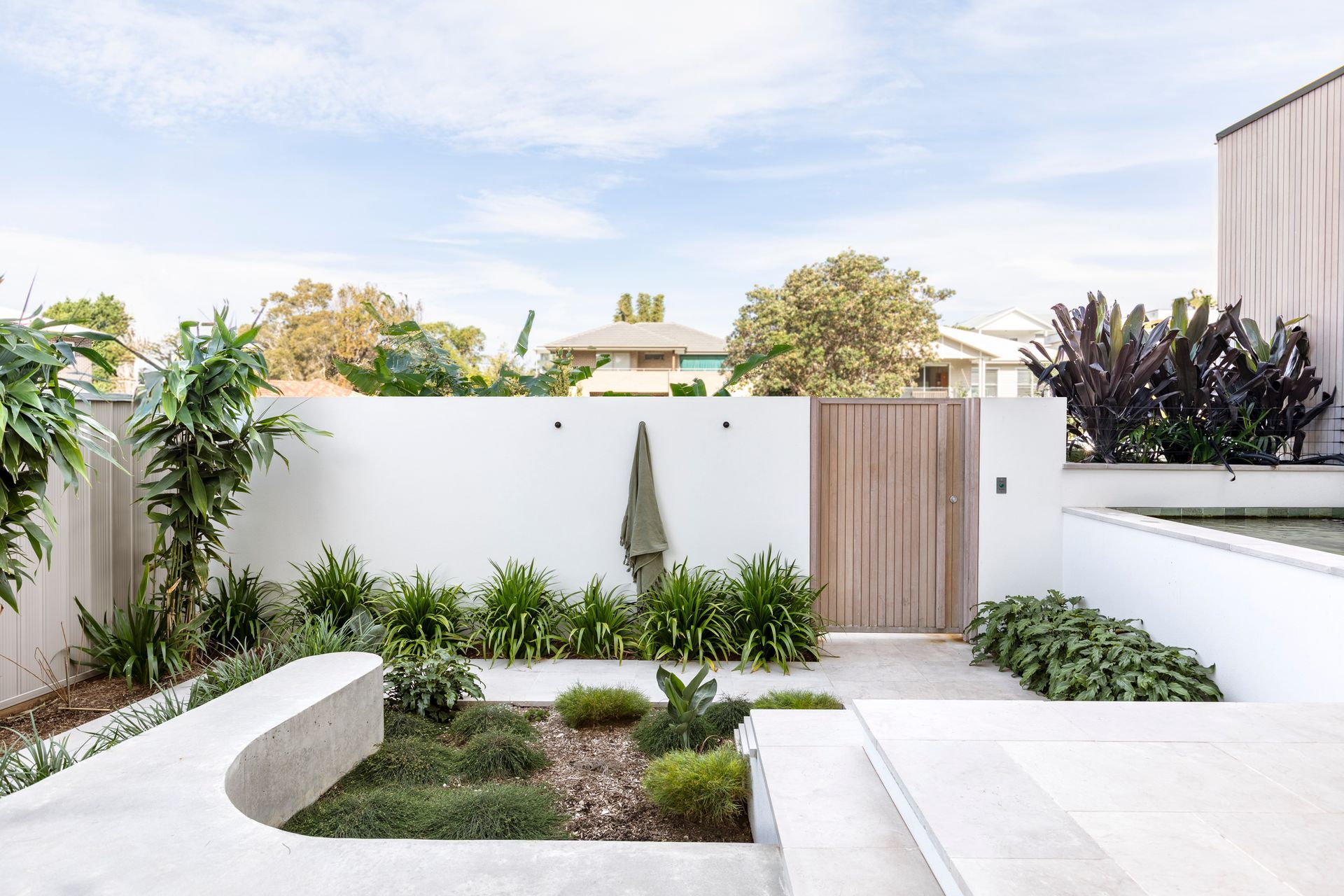White walled outdoor space with a wooden gate, lush greenery, and a curved concrete bench — Escarpment Building in Austinmer, NSW