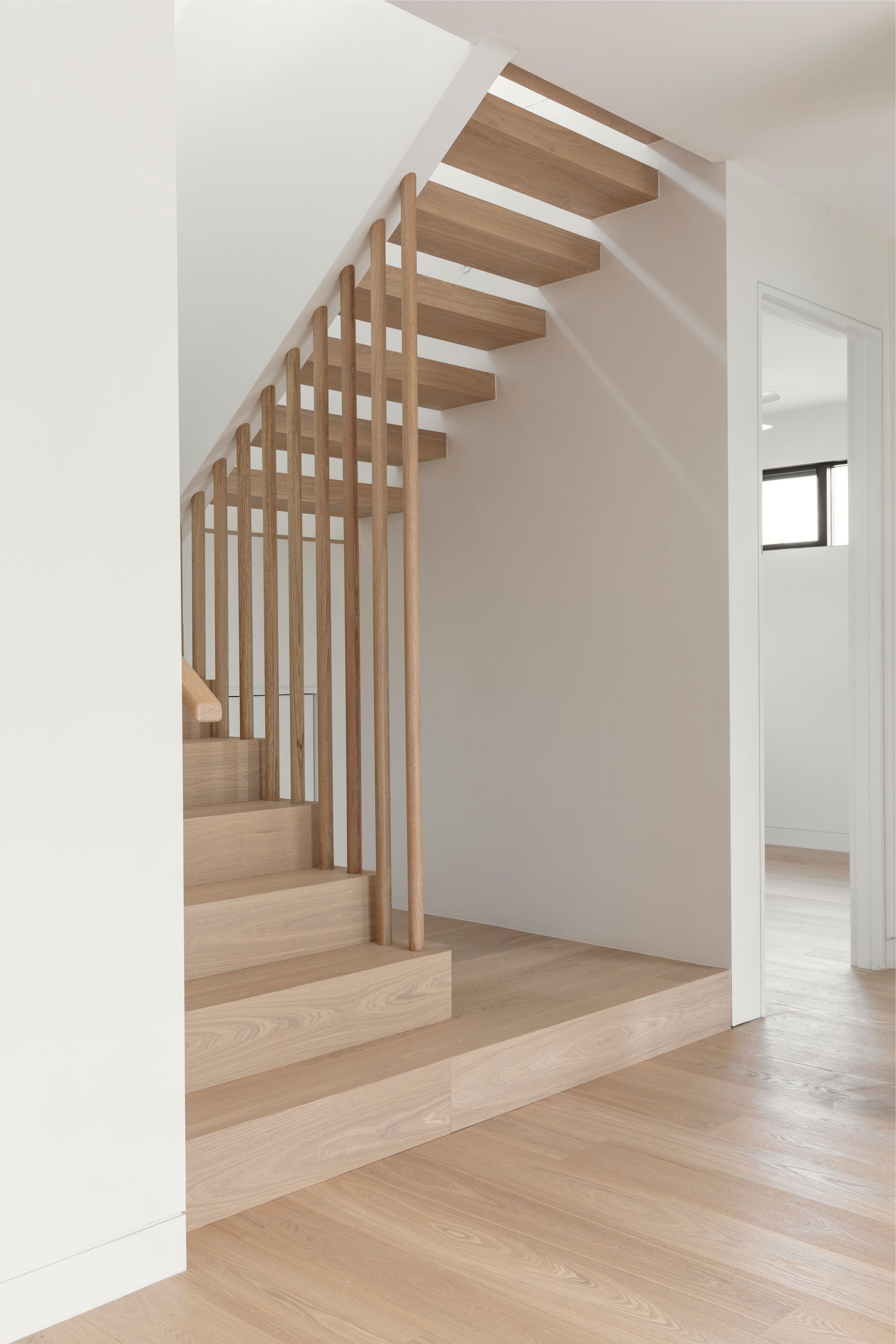 Wooden staircase with vertical railing against a white wall and light wood flooring — Escarpment Building in Austinmer, NSW