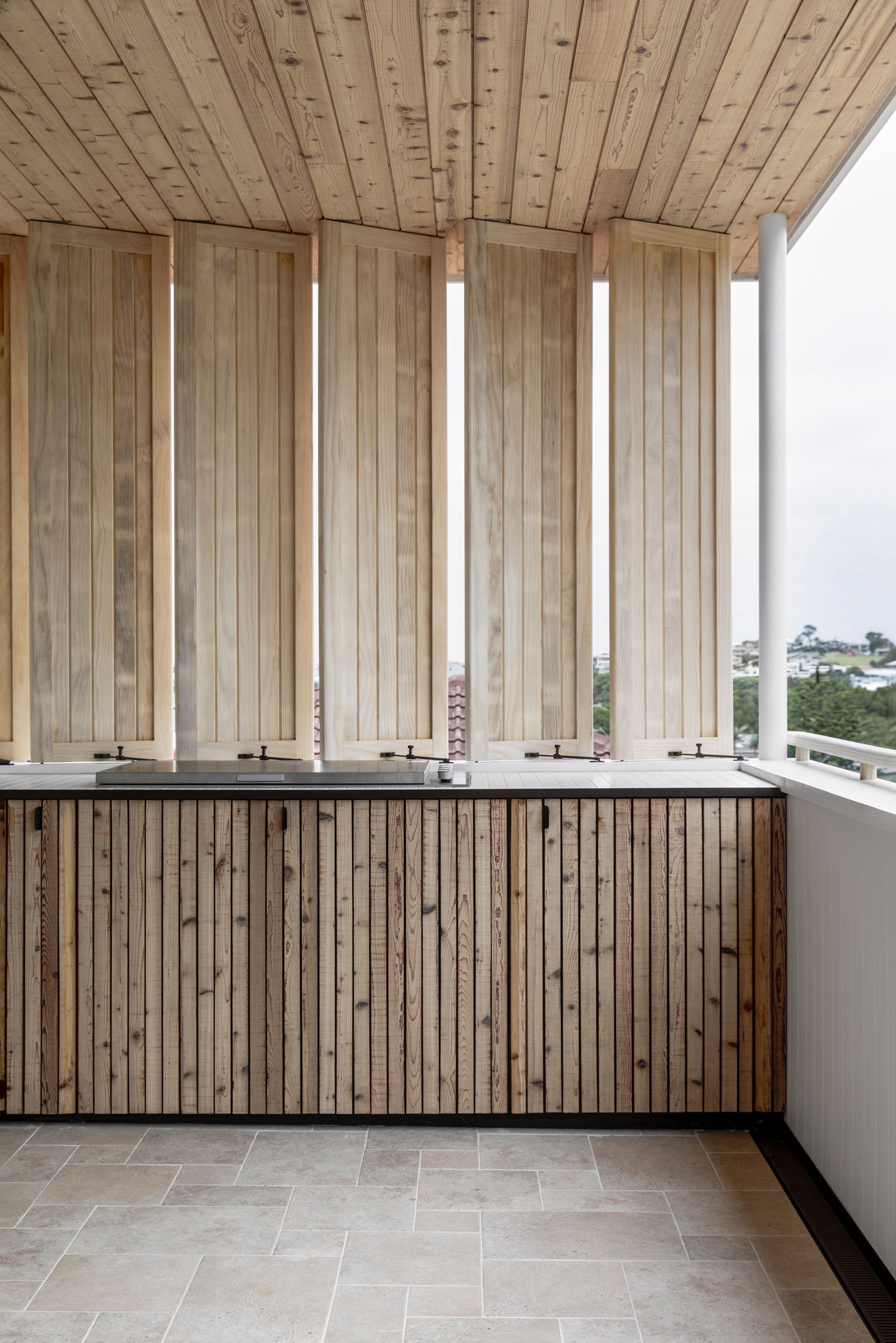 Wooden shutters on a balcony overlook a city. Light wood facade, concrete floor, white pillars — Escarpment Building in Austinmer, NSW