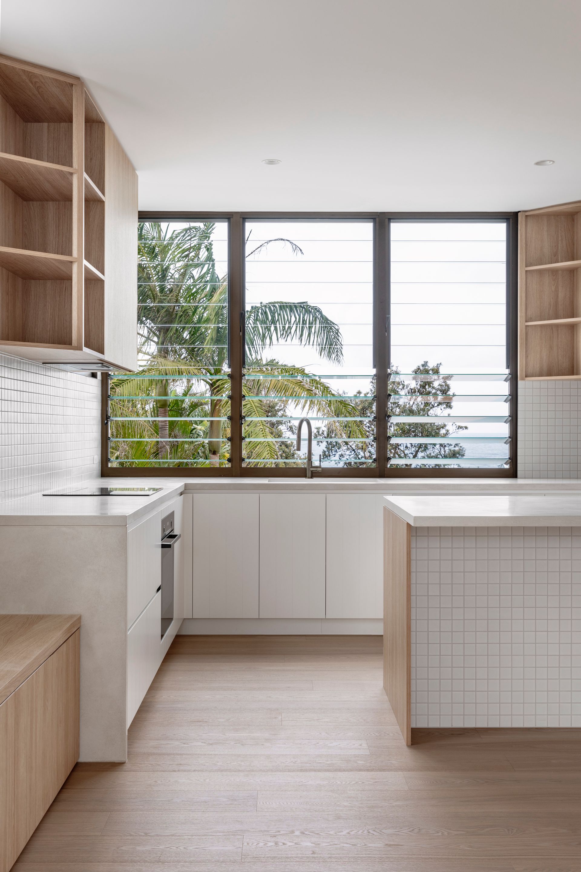 Modern white kitchen with wooden shelves, large window overlooking trees — Escarpment Building in Austinmer, NSW