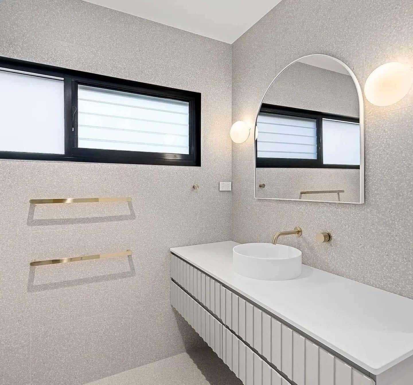 Bathroom with textured walls, floating vanity, arched mirror, and brass fixtures — Escarpment Building in Austinmer, NSW