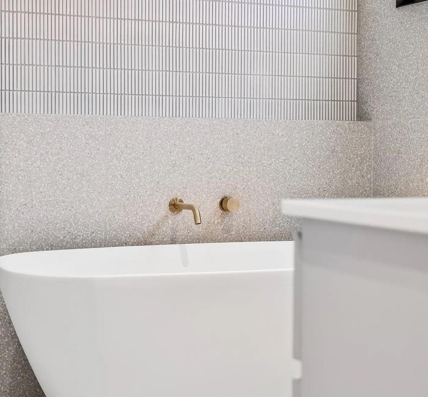 Bathtub with gold faucet against textured wall and vertical tile — Escarpment Building in Austinmer, NSW