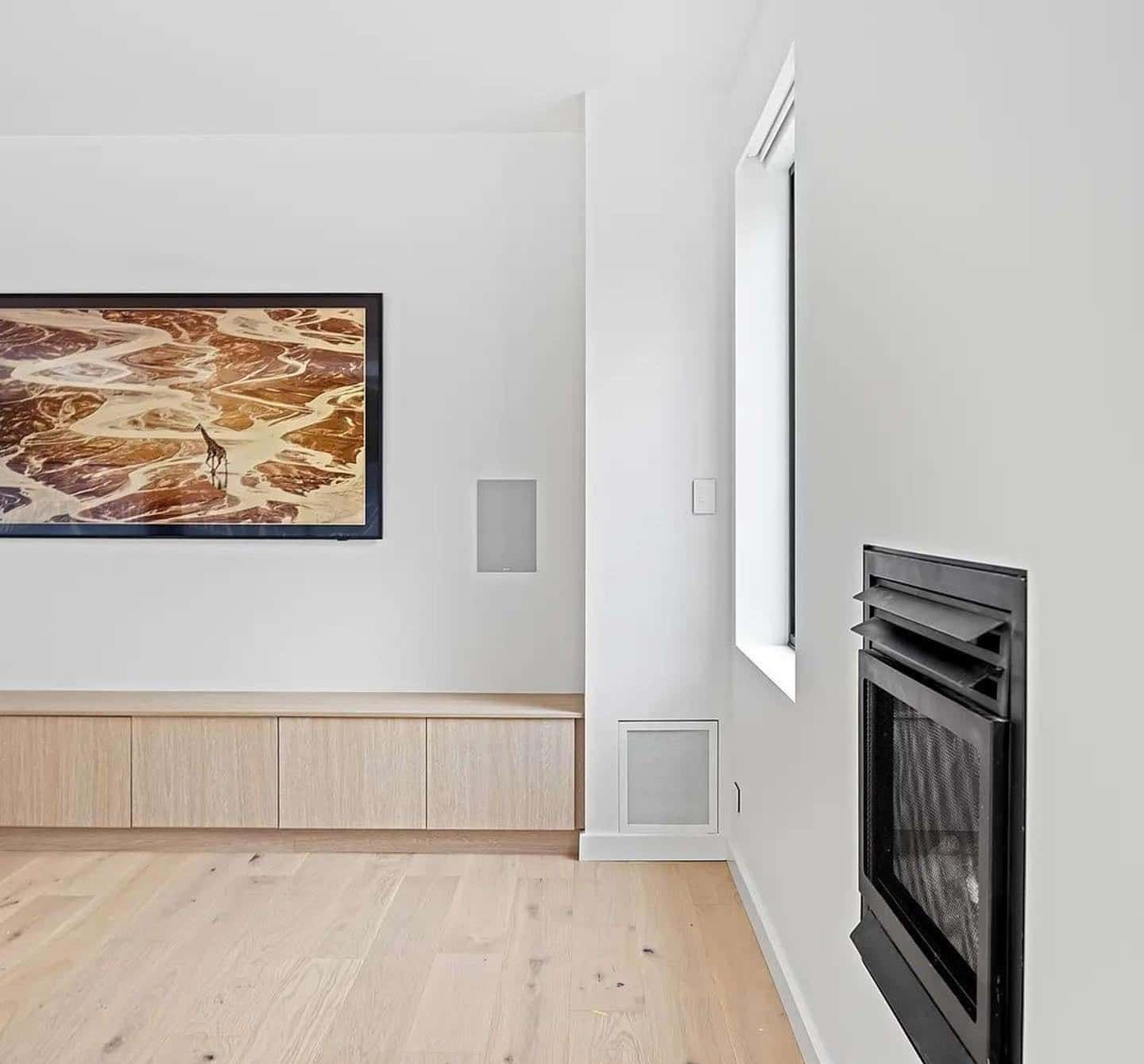 Modern white living room with light wood floors, a built-in cabinet, a framed artwork, and a fireplace — Escarpment Building in Austinmer, NSW
