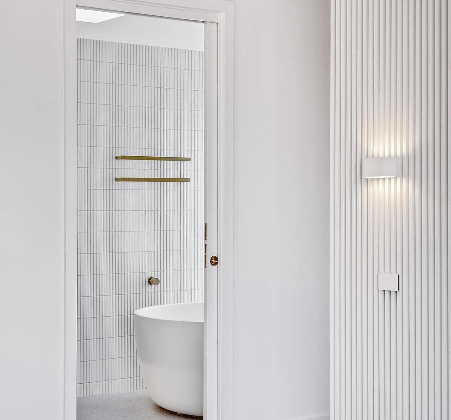 Bathroom interior with white walls, a bathtub, and vertical ribbed paneling — Escarpment Building in Austinmer, NSW