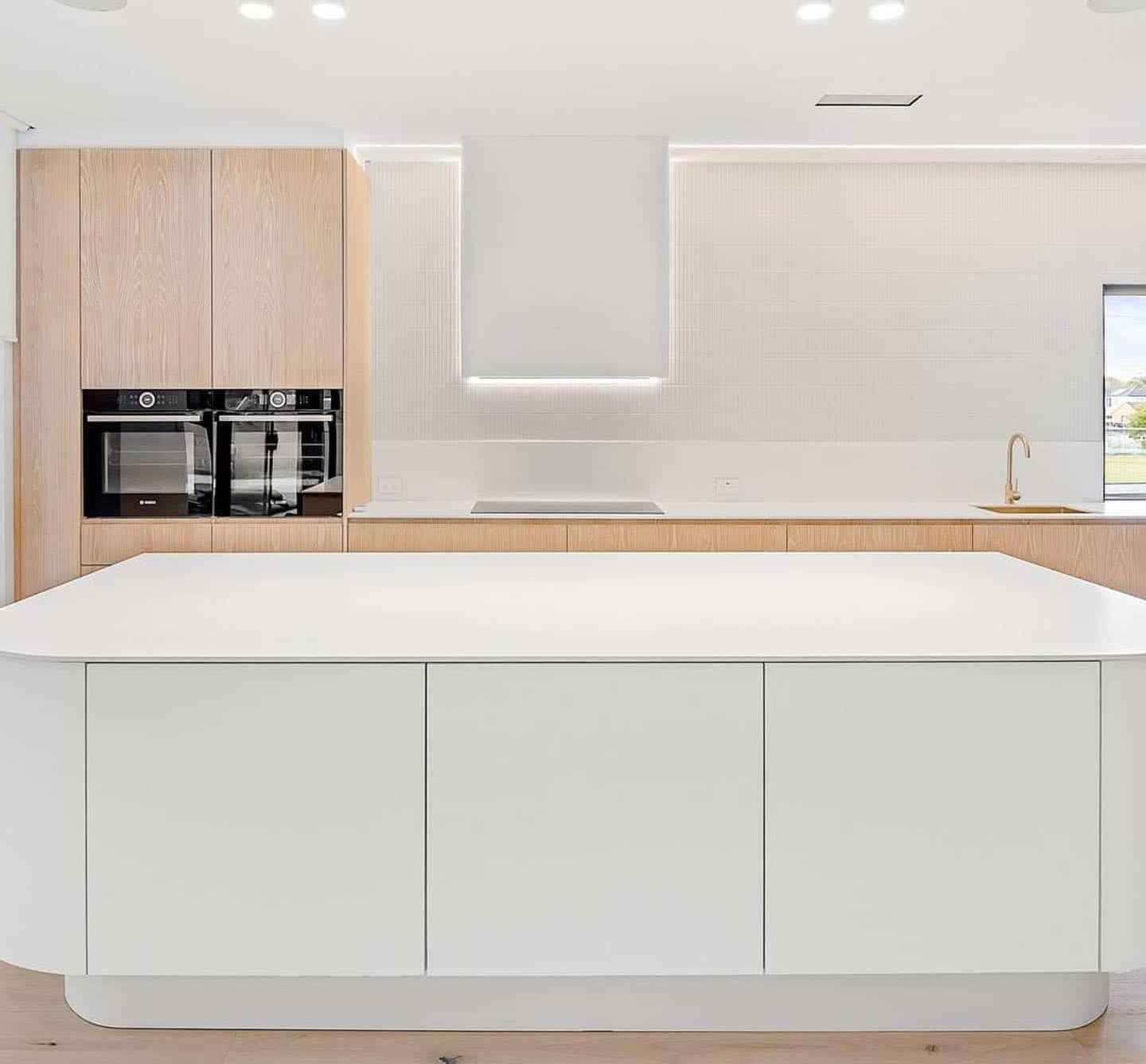Modern kitchen with white island, light wood cabinets, and white backsplash — Escarpment Building in Austinmer, NSW