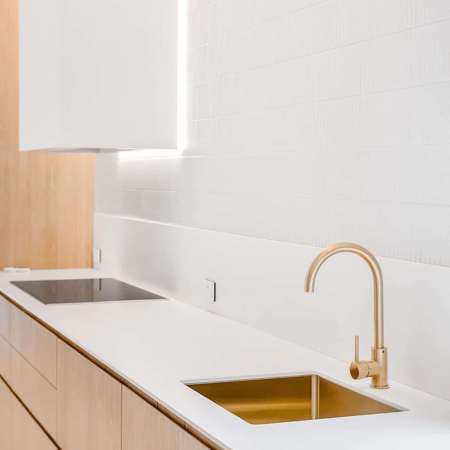 Modern kitchen with a gold faucet, sink, and white countertop against a white tiled wall — Escarpment Building in Austinmer, NSW
