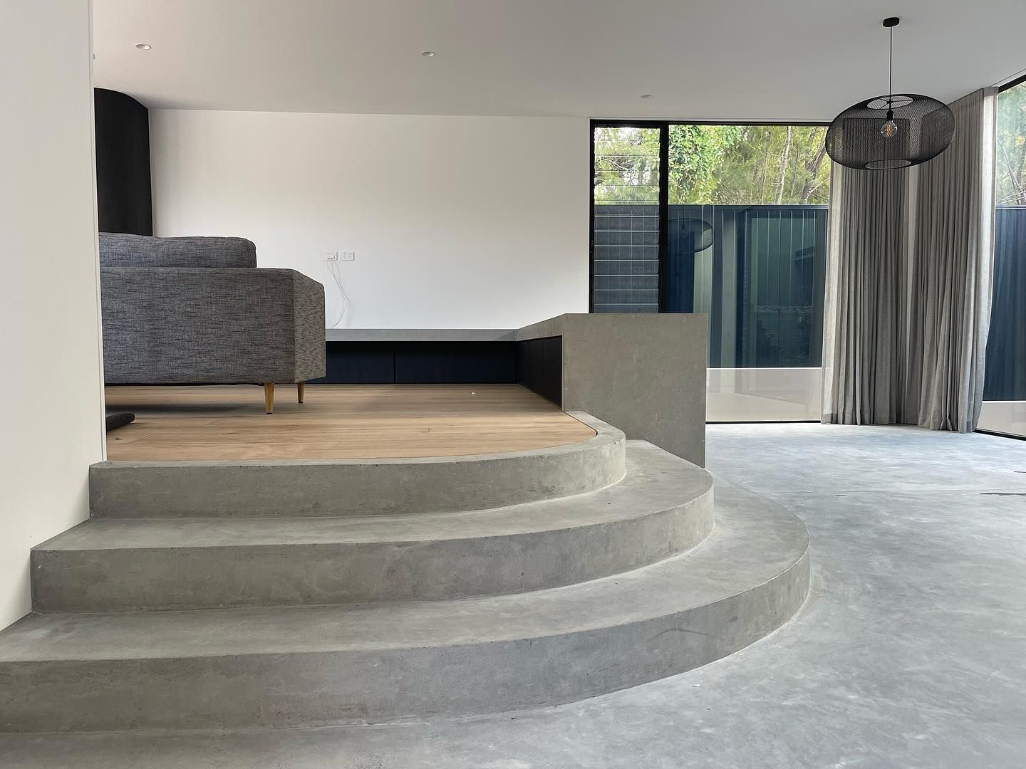 Concrete steps lead to a raised living area with a gray couch. Large windows with curtains are visible — Escarpment Building in Austinmer, NSW