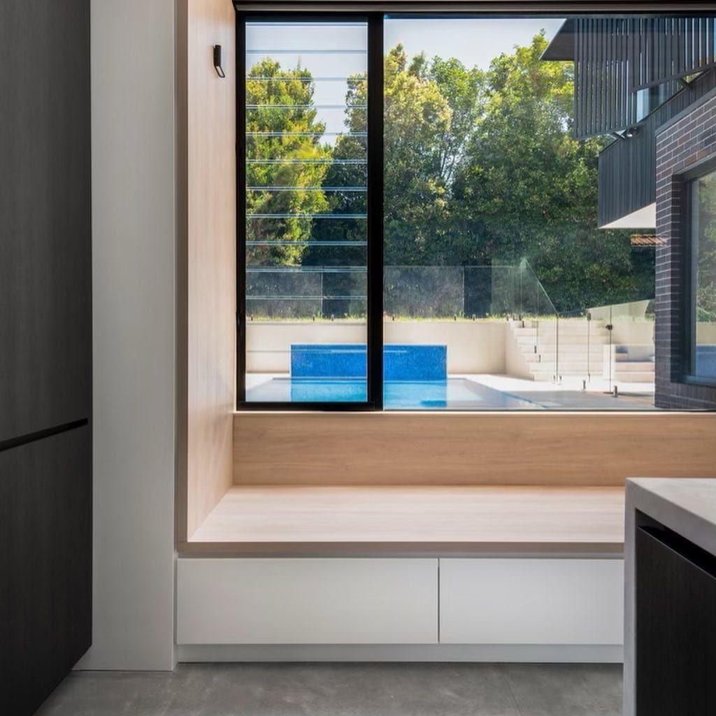 Interior shot with a window seat overlooking a pool and trees. The seat has white storage drawers — Escarpment Building in Austinmer, NSW