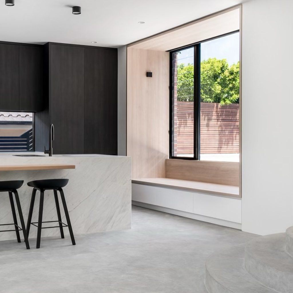 Modern kitchen with dark cabinetry, light-coloured island with stools, and a window seat overlooking a backyard — Escarpment Building in Austinmer, NSW