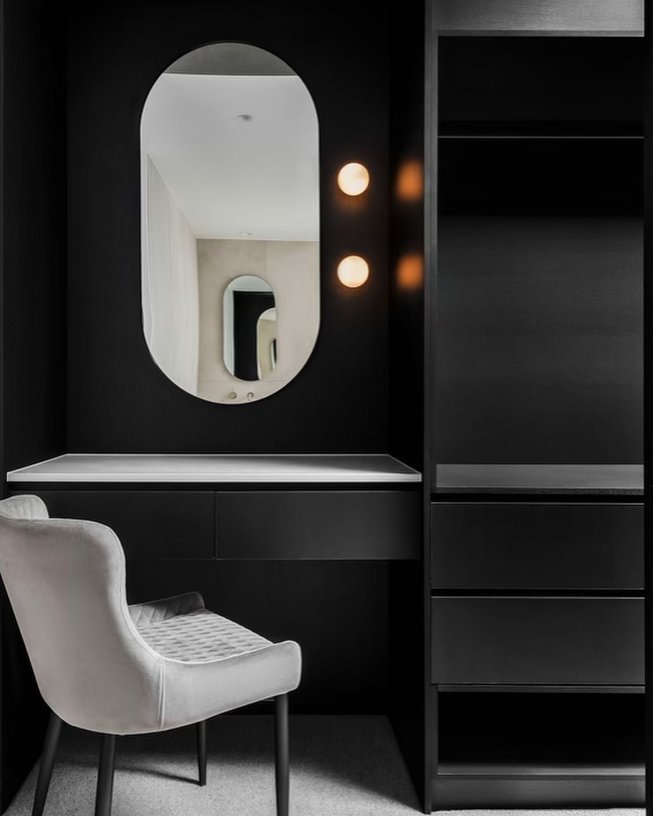 Black vanity with oval mirror, lights, built-in storage, and a light gray chair — Escarpment Building in Austinmer, NSW