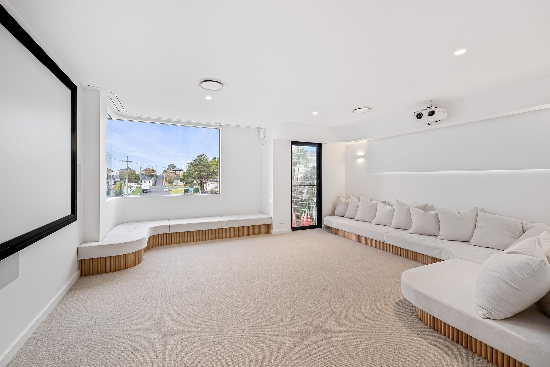 White home theater room with screen, seating, window, and projector — Escarpment Building in Austinmer, NSW