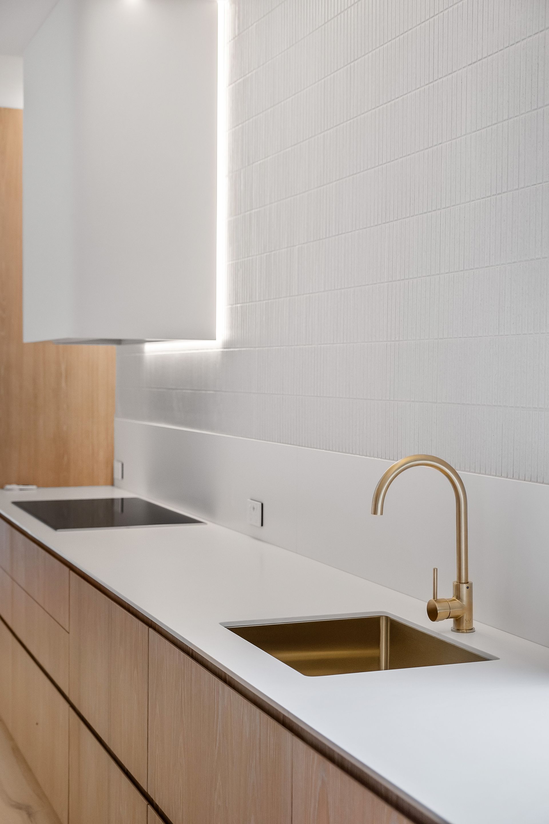Modern kitchen with wood cabinets, white countertops, and gold faucet over a stainless steel sink — Escarpment Building in Austinmer, NSW