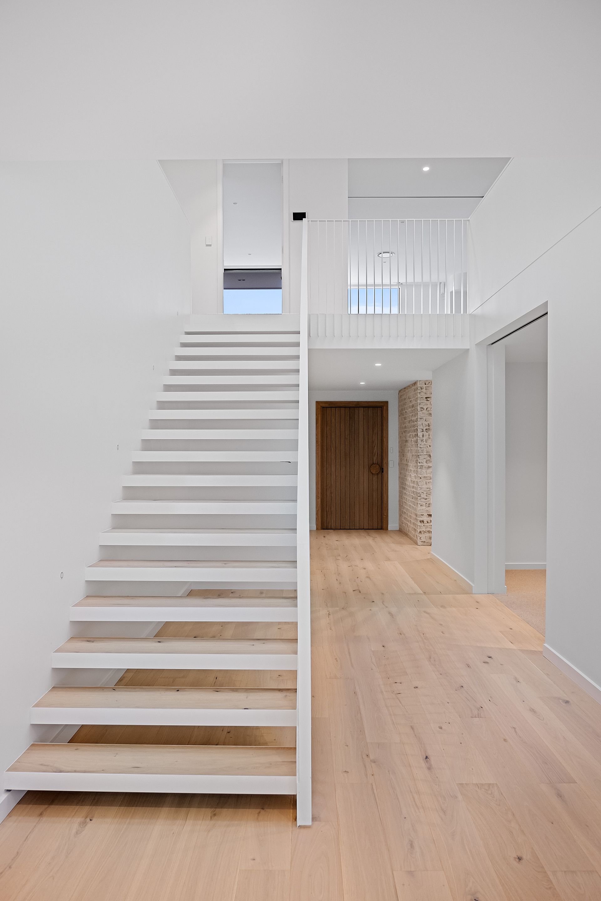 White staircase in a modern, light-filled interior. Light wood floors, natural wood door — Escarpment Building in Austinmer, NSW