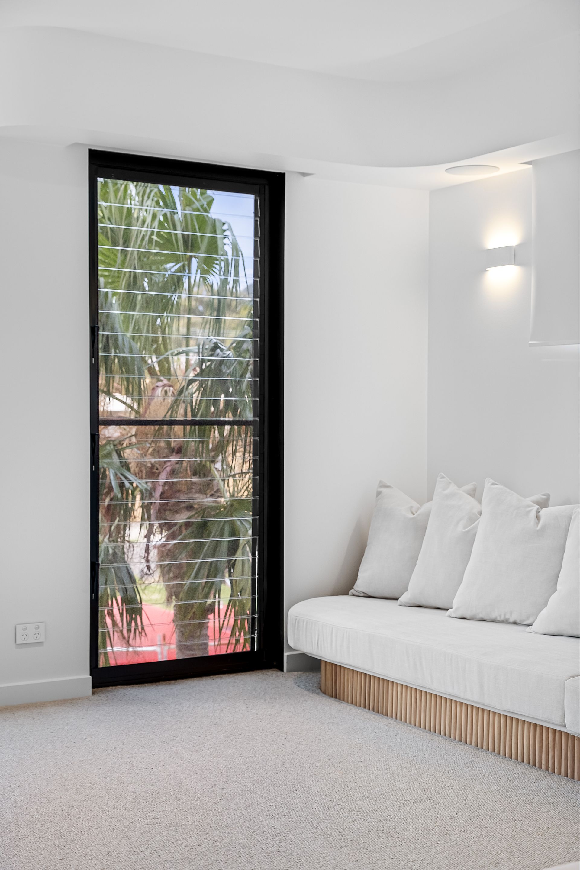 White-walled room with a tall black-framed window and a white couch. The room has a white carpet — Escarpment Building in Austinmer, NSW