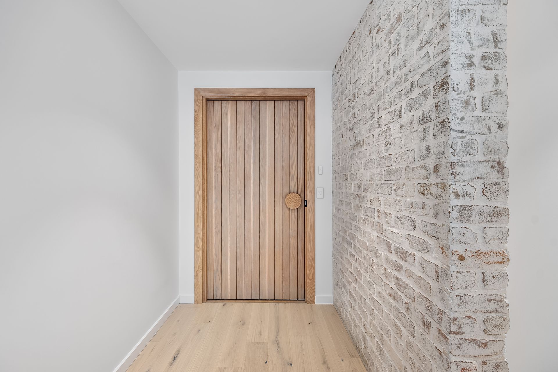 Wooden door in a hallway, framed by light brick wall on right, white walls and wood floor — Escarpment Building in Austinmer, NSW