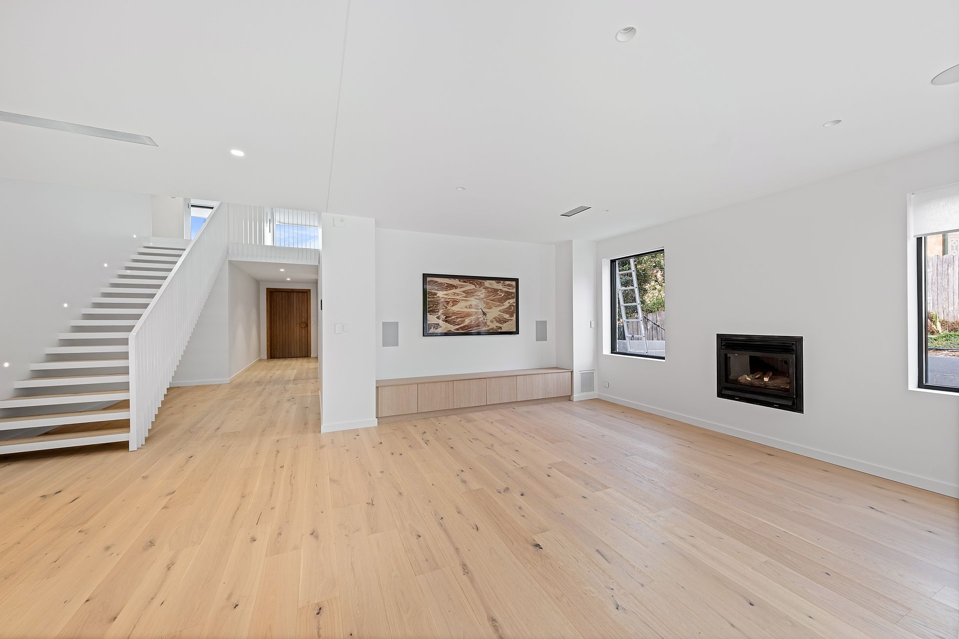 Spacious, bright living room with hardwood floors, white walls, staircase, and fireplace — Escarpment Building in Austinmer, NSW