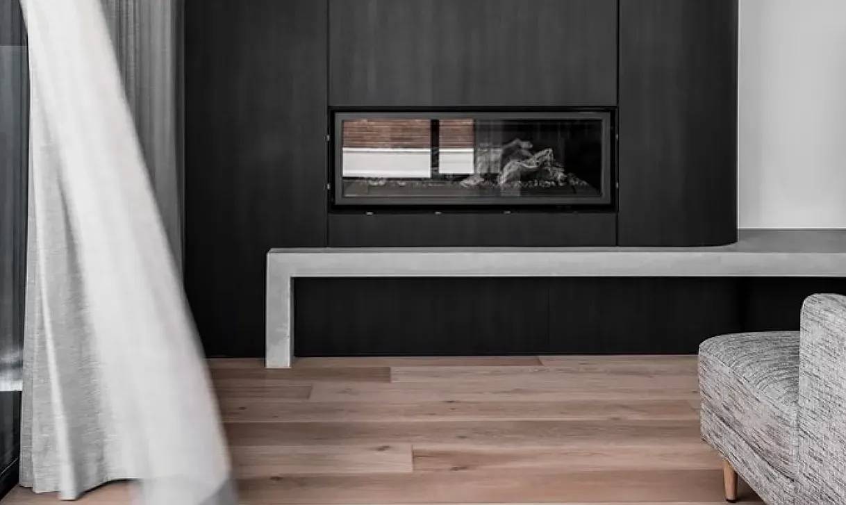 Modern living room with black fireplace, light wood floor, gray bench, and white curtain — Escarpment Building in Austinmer, NSW