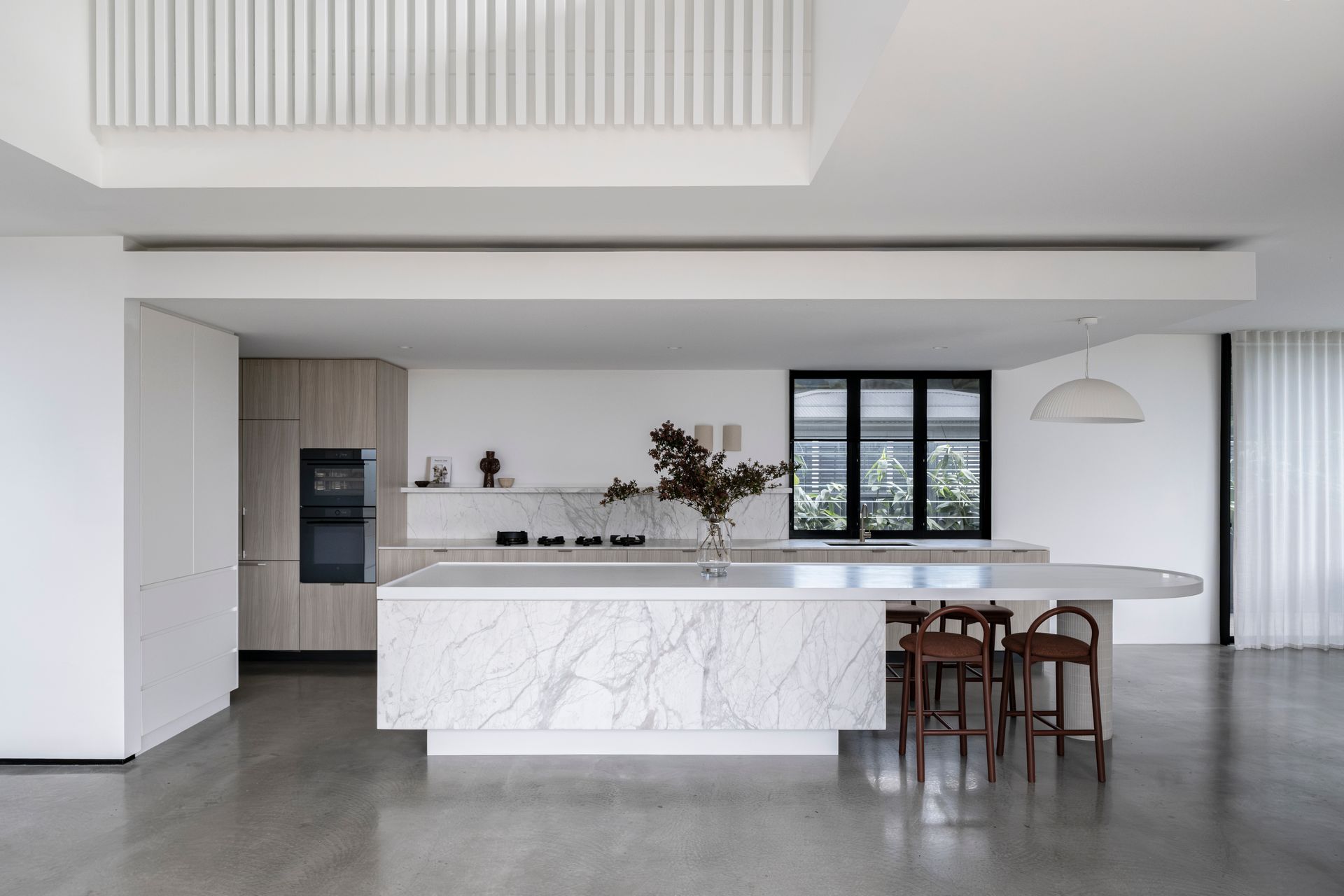 Modern white kitchen with marble island, wooden stools, and built-in appliances — Escarpment Building in Austinmer, NSW