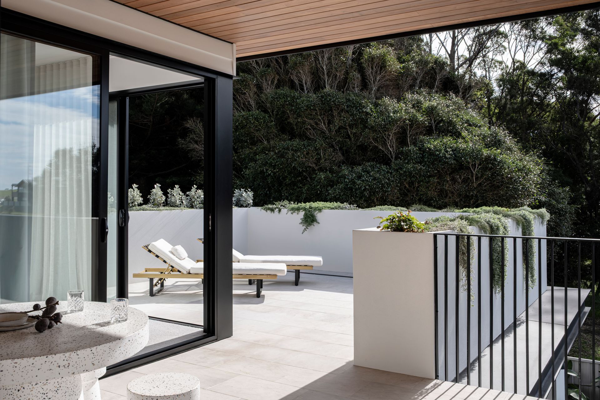 Balcony with lounge chairs, table, and sliding glass door, overlooking greenery — Escarpment Building in Austinmer, NSW